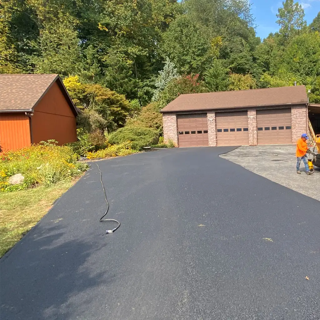 Freshly sealcoated asphalt driveway leading to a three-car residential garage.